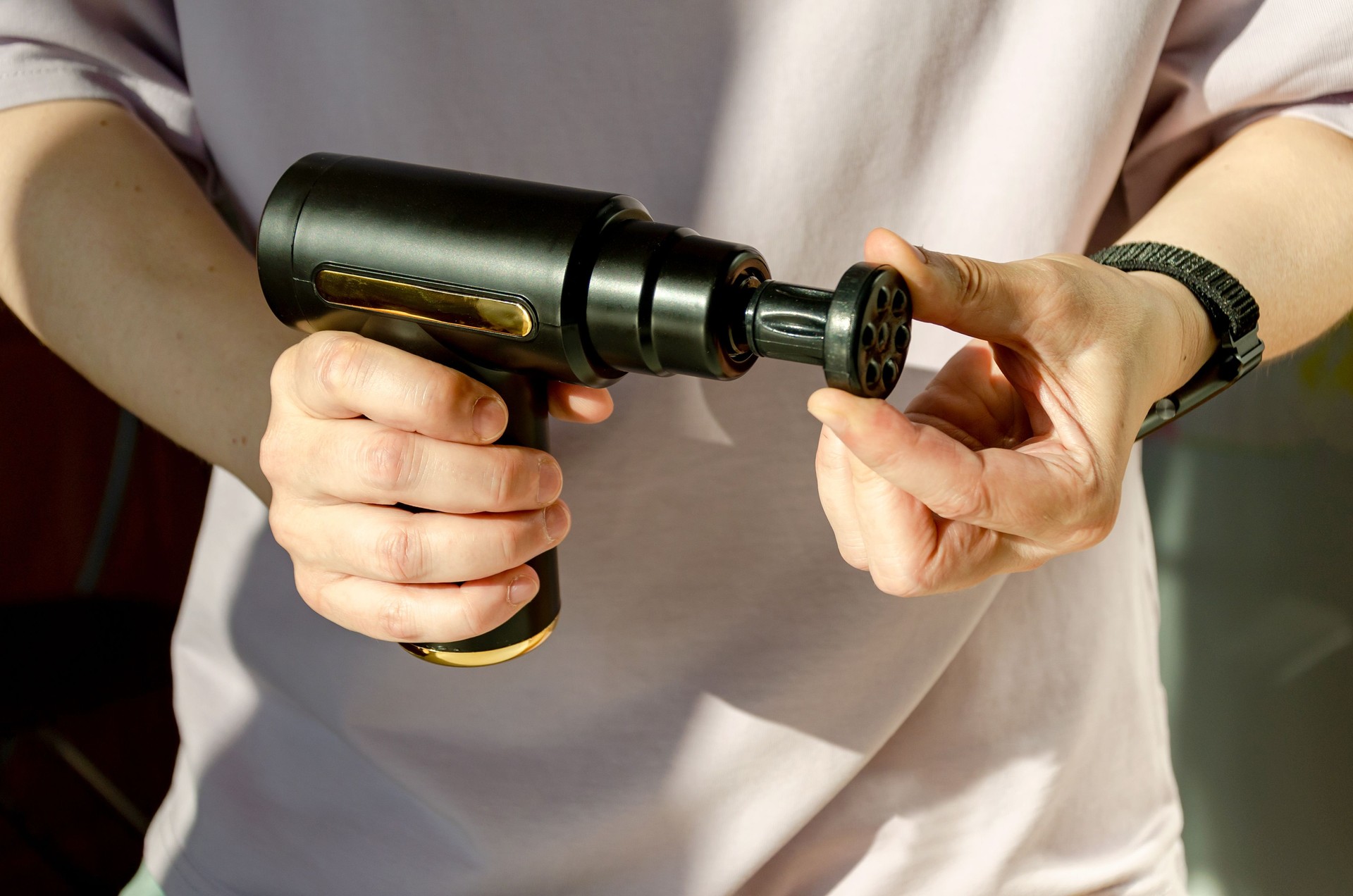 Woman holding portable massage gun, demonstrating changing attachments.